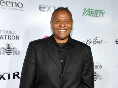 Damon Whitaker is wearing a black suit, shirt, and tie.